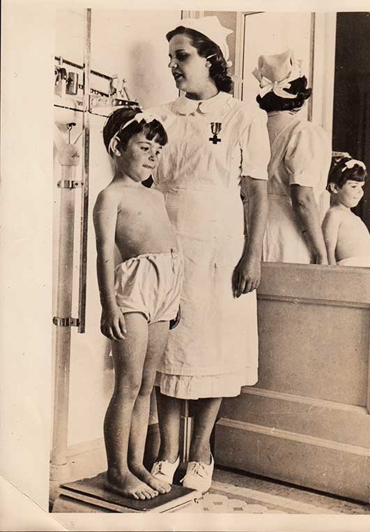 Fotografía. "Hija de la nueva España". Niña huérfana de la guerra civil que es medida por una enfermera